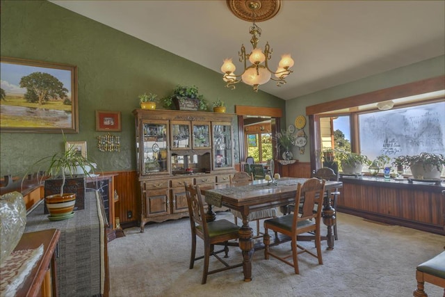 carpeted dining space with a notable chandelier, vaulted ceiling, and wood walls