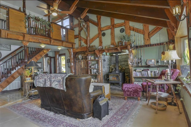 living room featuring beamed ceiling, ceiling fan, a wood stove, and high vaulted ceiling