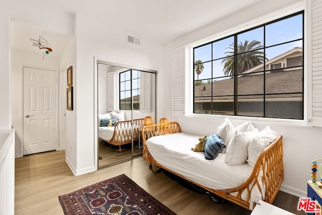 bedroom with a closet, light hardwood / wood-style floors, and multiple windows