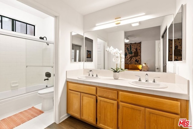 full bathroom with toilet, ceiling fan, vanity, and bath / shower combo with glass door