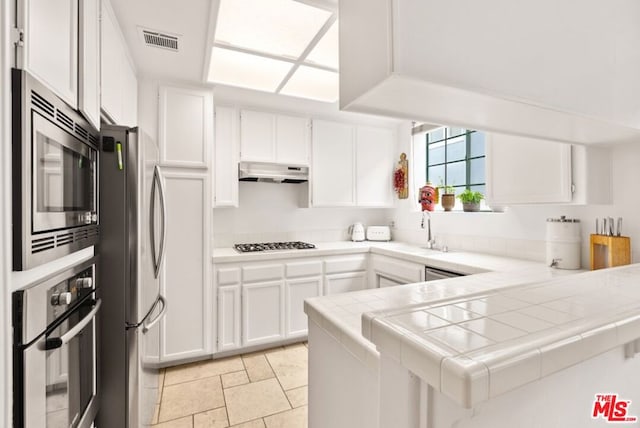 kitchen featuring sink, tile counters, kitchen peninsula, stainless steel appliances, and white cabinets