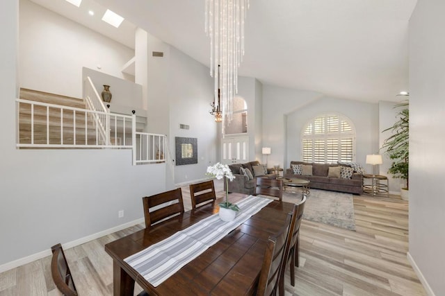 dining space with a skylight, high vaulted ceiling, a chandelier, and light hardwood / wood-style flooring