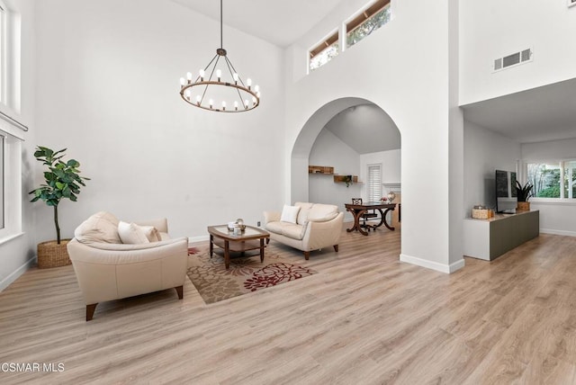 living room featuring a towering ceiling, a chandelier, and light wood-type flooring