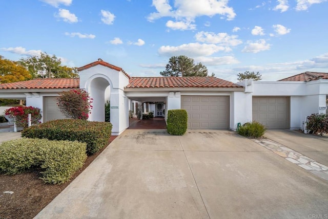 mediterranean / spanish-style house featuring a garage, a tile roof, concrete driveway, and stucco siding