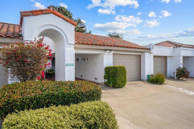 mediterranean / spanish house with a garage, concrete driveway, a tiled roof, and stucco siding