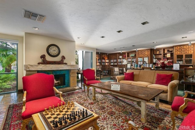 living room featuring built in features, a fireplace, visible vents, and a textured ceiling