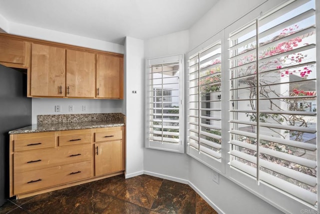 kitchen featuring dark stone countertops, plenty of natural light, freestanding refrigerator, and baseboards