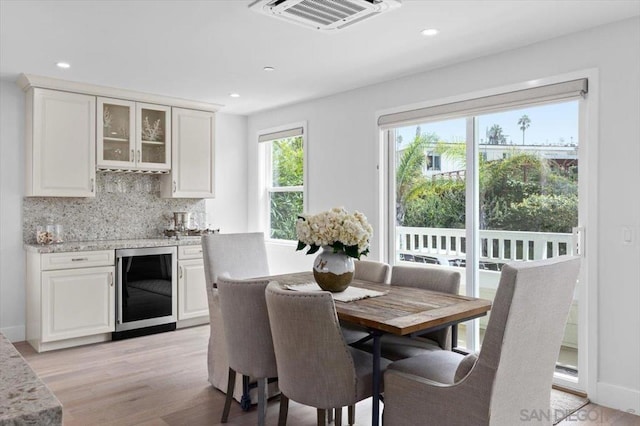 dining space with indoor bar, beverage cooler, and light wood-type flooring