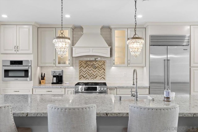 kitchen with stainless steel appliances, decorative light fixtures, light stone countertops, and custom range hood