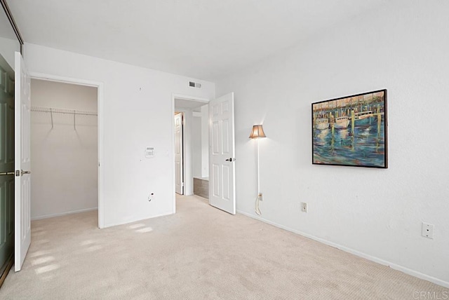 unfurnished bedroom with a walk in closet, light colored carpet, and a closet