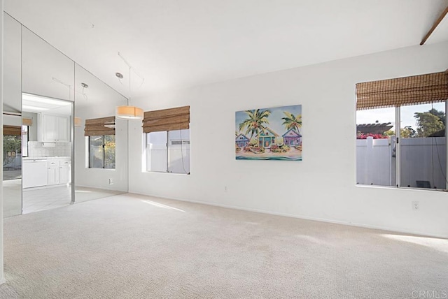 unfurnished room with lofted ceiling, light colored carpet, and a healthy amount of sunlight