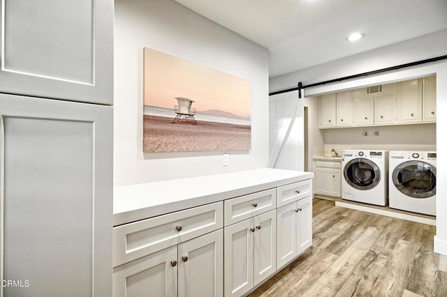 washroom featuring sink, washing machine and dryer, cabinets, a barn door, and light hardwood / wood-style floors