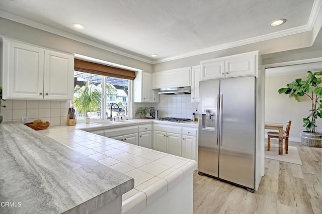 kitchen featuring tile counters, a peninsula, white cabinets, stainless steel appliances, and a sink