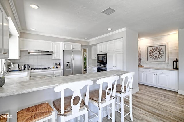 kitchen with a kitchen breakfast bar, stainless steel fridge, under cabinet range hood, gas stovetop, and a sink
