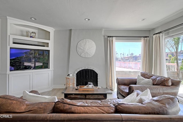 living room featuring a large fireplace, built in shelves, recessed lighting, and wood finished floors