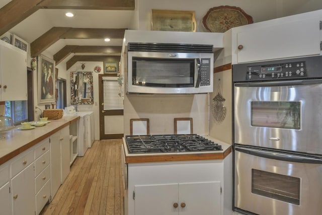 kitchen with lofted ceiling, washer / dryer, light hardwood / wood-style flooring, appliances with stainless steel finishes, and white cabinets