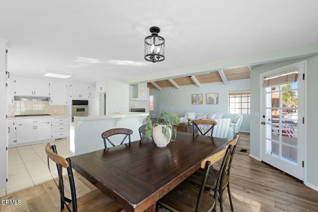 dining space featuring vaulted ceiling with beams, a chandelier, and light hardwood / wood-style floors