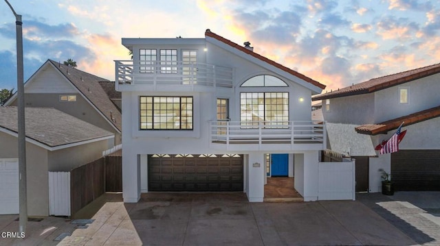 back house at dusk featuring a garage and a balcony