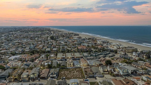 aerial view at dusk featuring a water view and a beach view