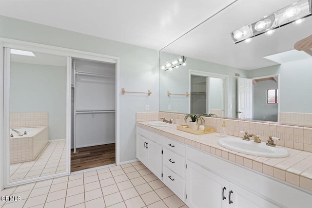 bathroom featuring tile patterned flooring, tiled tub, vanity, and tasteful backsplash