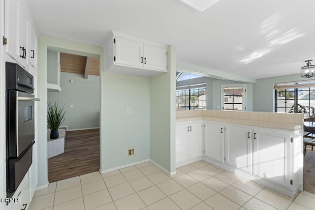 kitchen with tile countertops, light tile patterned floors, kitchen peninsula, double oven, and white cabinets