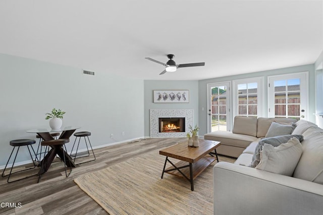 living room featuring hardwood / wood-style floors, a tile fireplace, and ceiling fan