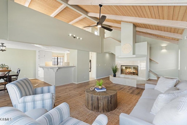 living room with beam ceiling, a tile fireplace, wood ceiling, and light hardwood / wood-style floors