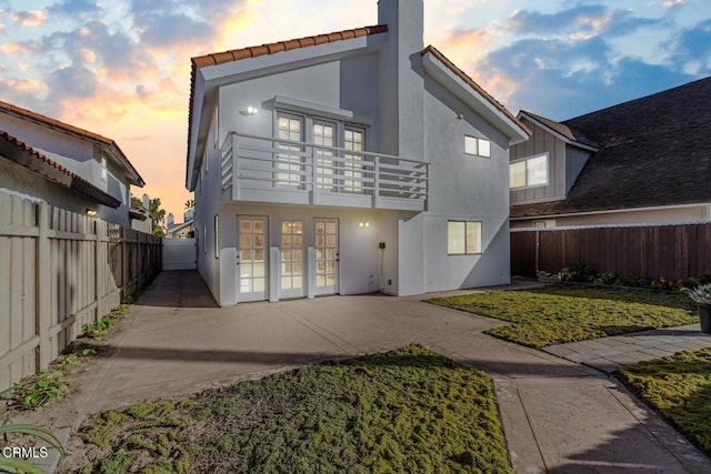 back house at dusk featuring a patio area, french doors, and a balcony