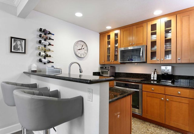 kitchen with sink, dark stone countertops, appliances with stainless steel finishes, a kitchen breakfast bar, and kitchen peninsula