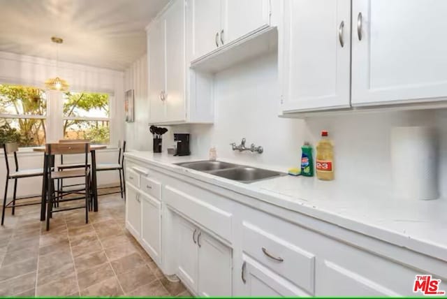 kitchen with sink, decorative light fixtures, light stone countertops, and white cabinets