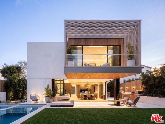 back house at dusk with a yard, a patio, area for grilling, an outdoor living space with a fire pit, and a balcony