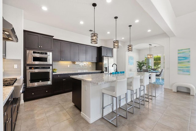 kitchen with extractor fan, a kitchen breakfast bar, hanging light fixtures, light stone counters, and a center island with sink