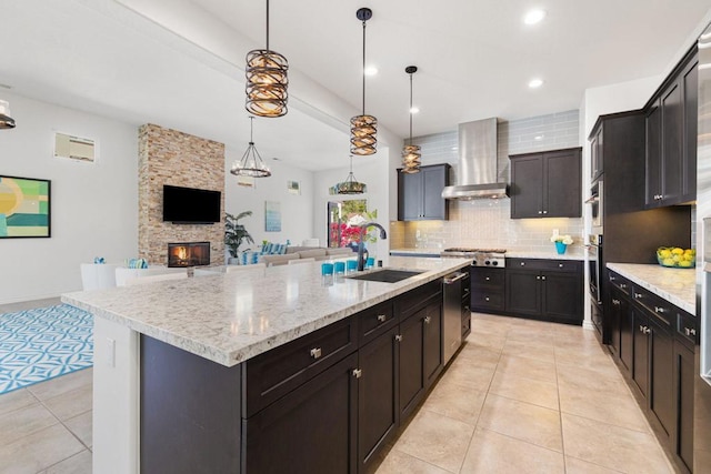 kitchen with a large island, sink, hanging light fixtures, wall chimney exhaust hood, and stainless steel gas stovetop