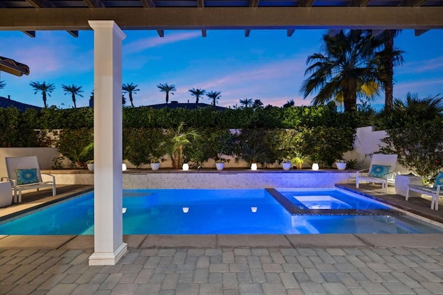 pool at dusk with an in ground hot tub and a patio area