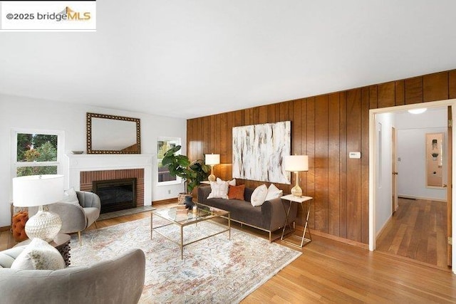 living room featuring a brick fireplace, wooden walls, and light wood-type flooring