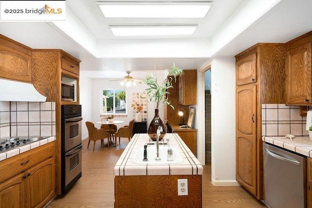 kitchen featuring appliances with stainless steel finishes, a kitchen island, tile countertops, a raised ceiling, and light wood-type flooring