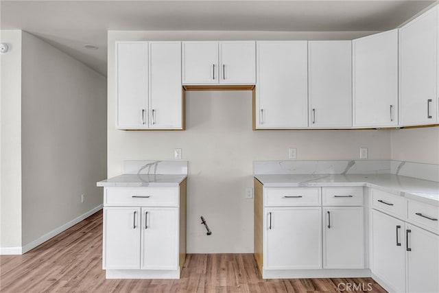 kitchen with white cabinets, light stone counters, and light hardwood / wood-style floors