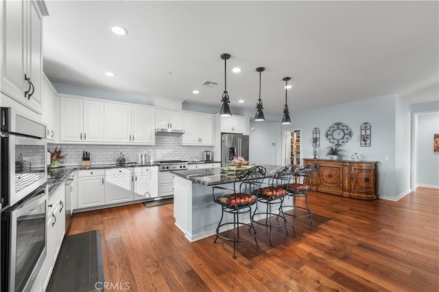 kitchen with a breakfast bar area, white cabinetry, hanging light fixtures, stainless steel appliances, and a kitchen island