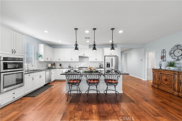 kitchen featuring pendant lighting, a breakfast bar, white cabinetry, stainless steel appliances, and a kitchen island