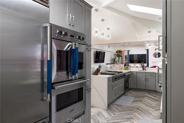 kitchen with gray cabinets, pendant lighting, stainless steel gas stovetop, light parquet flooring, and designer fridge