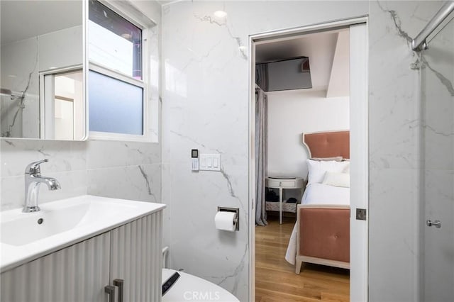 bathroom featuring hardwood / wood-style flooring, tile walls, vanity, a shower, and toilet