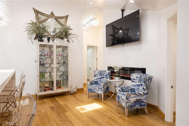 sitting room featuring an inviting chandelier, a towering ceiling, and wood-type flooring