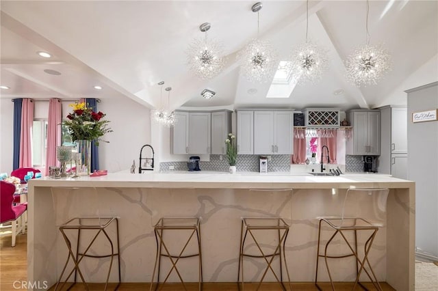 kitchen with a kitchen breakfast bar, decorative light fixtures, vaulted ceiling, and gray cabinetry