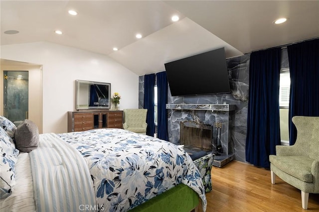 bedroom with a premium fireplace, vaulted ceiling, and hardwood / wood-style floors