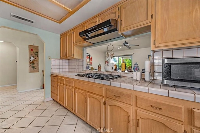 kitchen with ceiling fan, appliances with stainless steel finishes, backsplash, light tile patterned flooring, and tile countertops