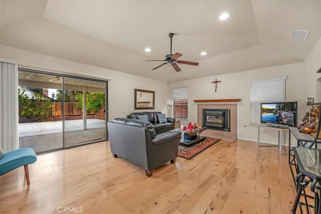 living room featuring a raised ceiling, a tile fireplace, ceiling fan, and light hardwood / wood-style floors