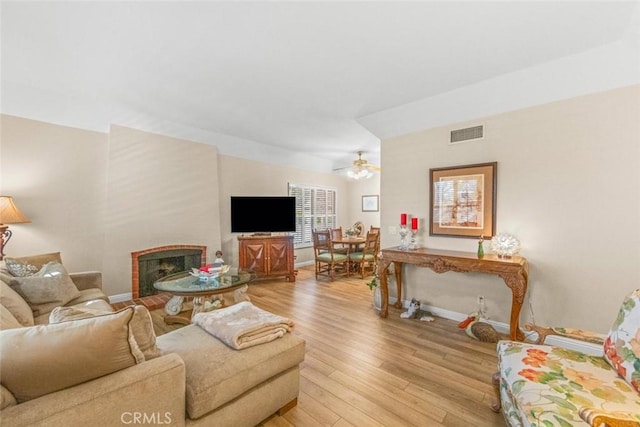 living room featuring ceiling fan, a fireplace, and light hardwood / wood-style flooring