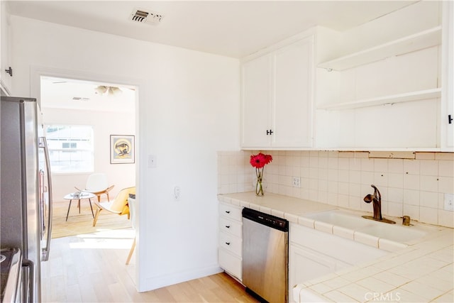 kitchen with sink, white cabinetry, tile countertops, stainless steel appliances, and backsplash