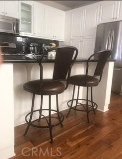 bar featuring stainless steel appliances, dark wood-style flooring, and backsplash