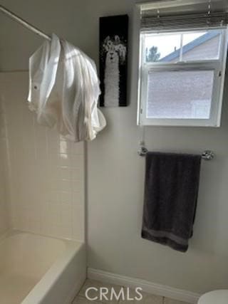 full bathroom with bathing tub / shower combination, toilet, and baseboards